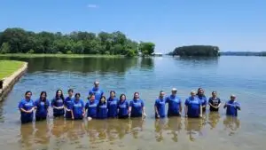 Eighteen men and women stand in a lake after being baptized.