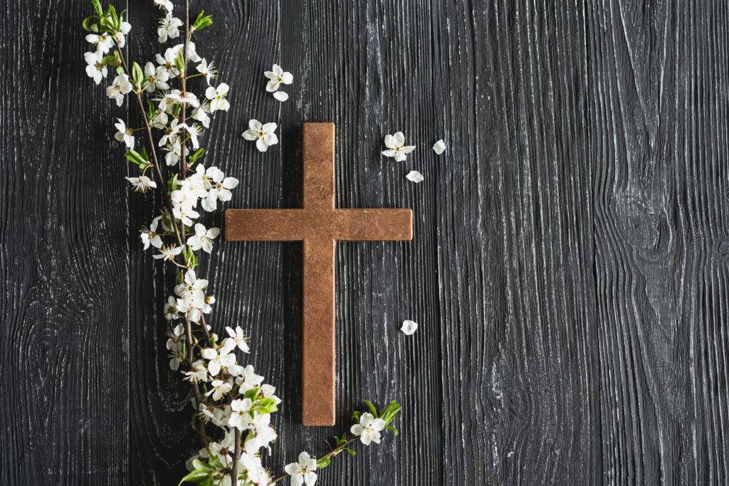 Easter cross, symbolizing the death and resurrection of Jesus Christ, spring flowers on a wood background.