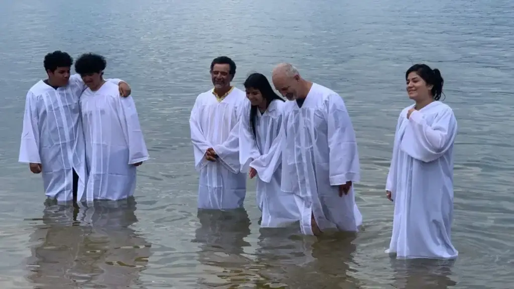 Hispanic churchgoers in white robes participate in a River Baptism