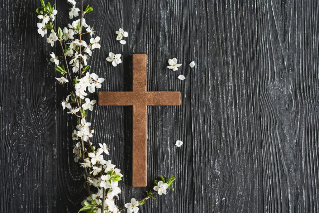 Cross symbolizing the death and resurrection of Jesus Christ, spring flowers on a wood background