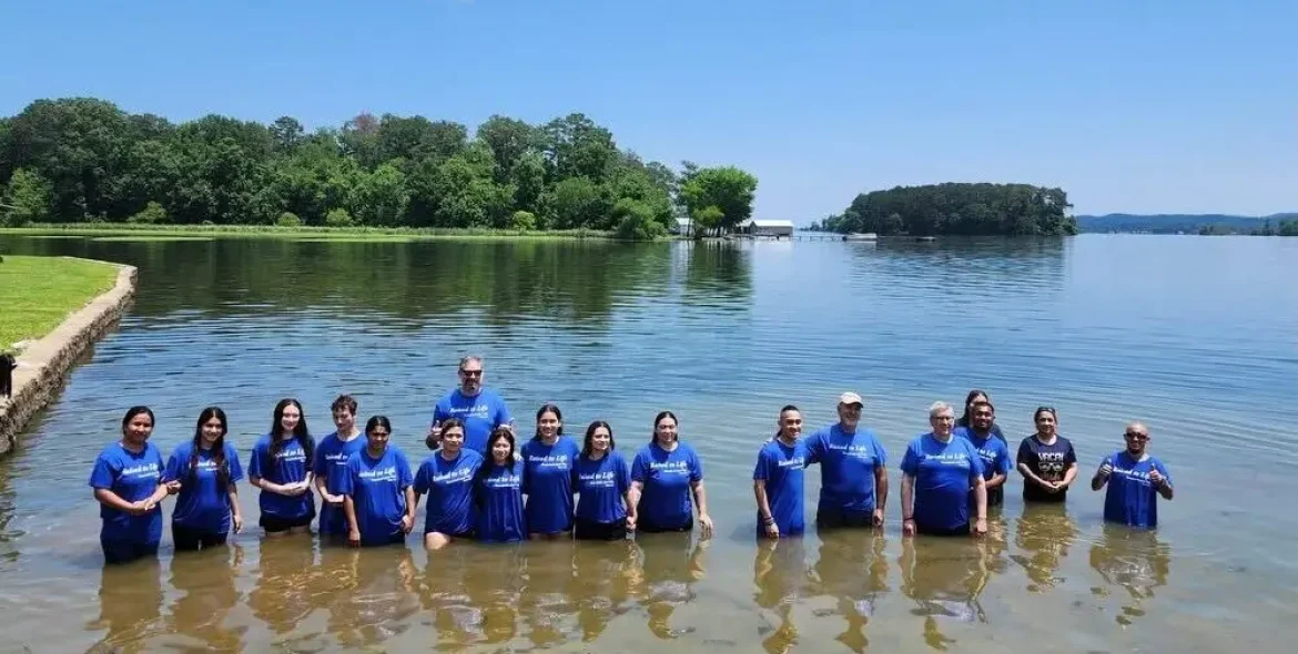 Eighteen men and women stand in a lake after being baptized.