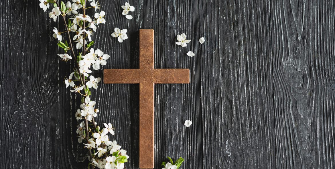 Easter cross, symbolizing the death and resurrection of Jesus Christ, spring flowers on a wood background.